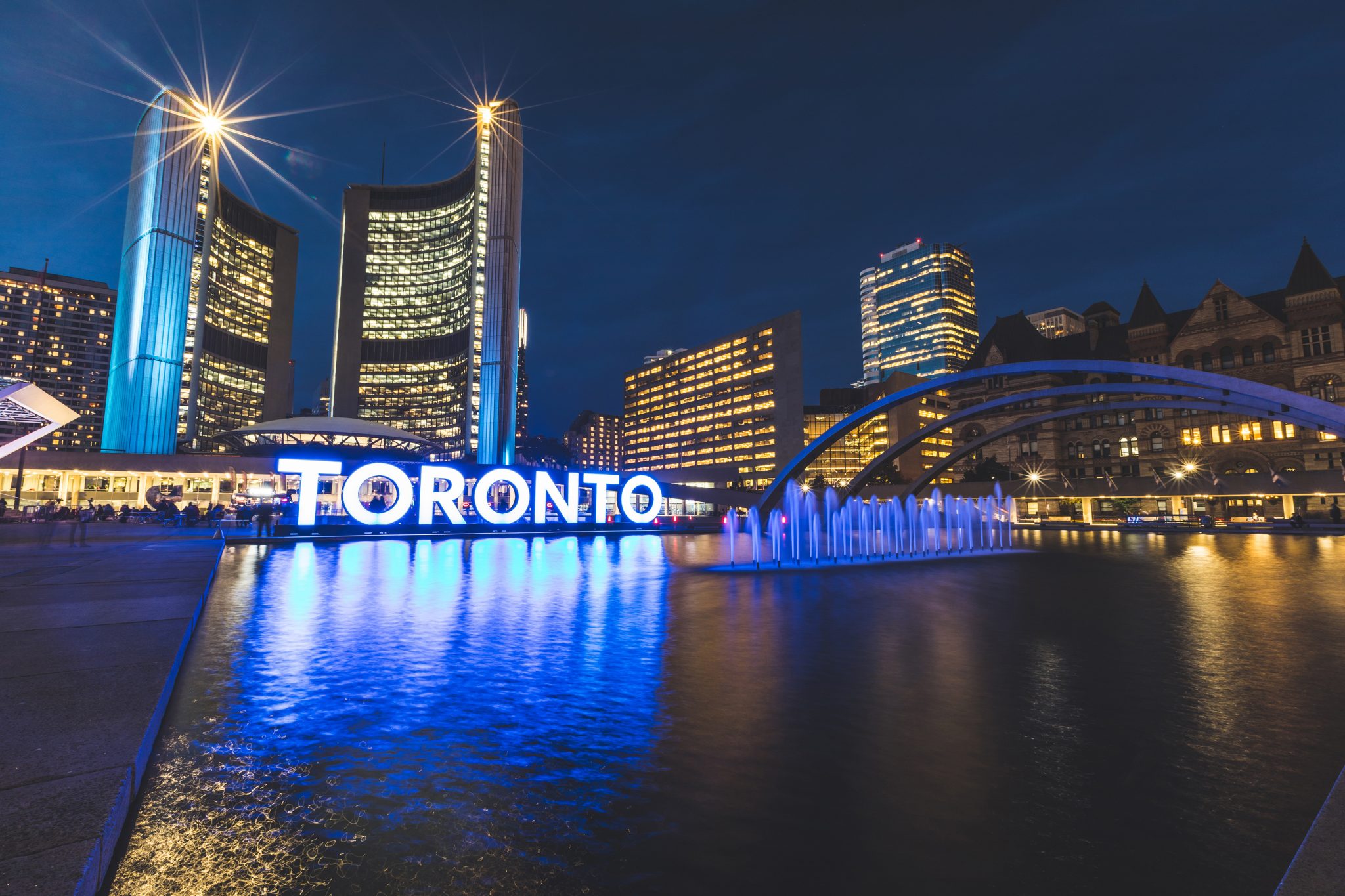 Image of Toronto City Hall and Toronto sign lit up at night.